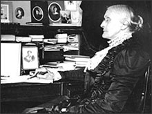 Susan B. Anthony sitting at desk with pen in hand.