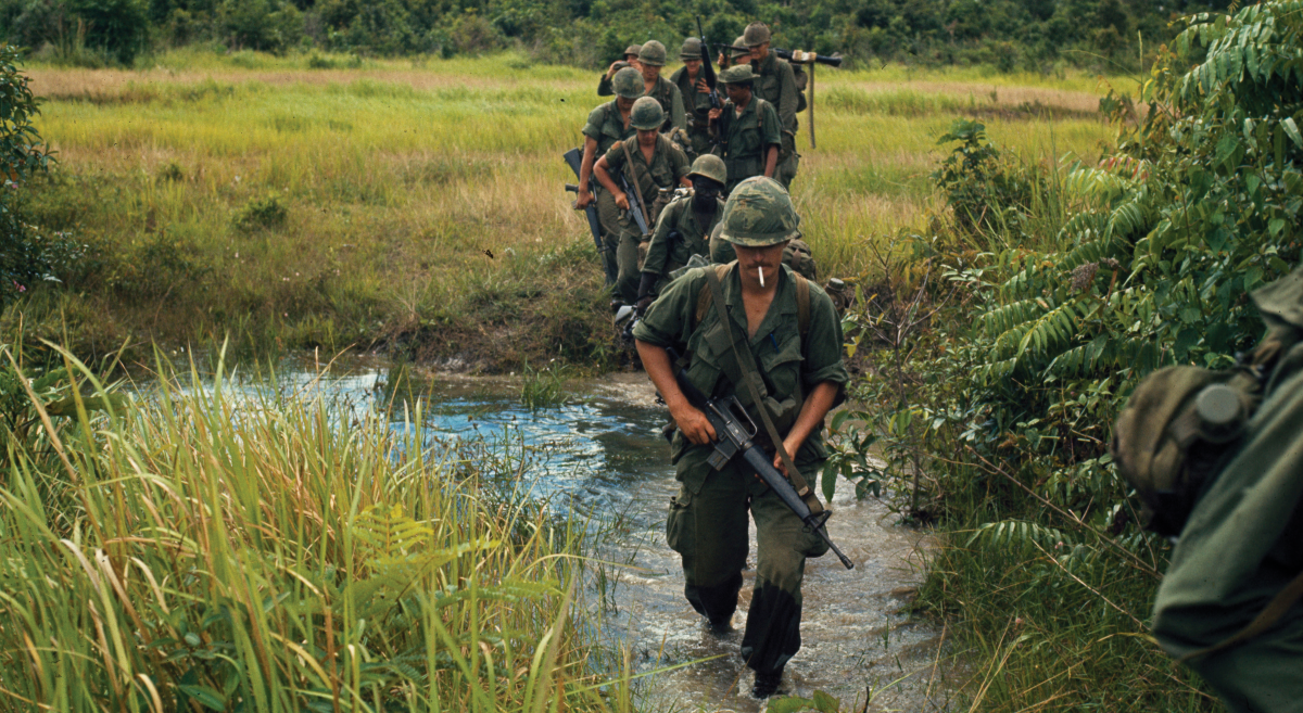 Solider's marching through a rice paddy Members of Company B, 1st Battalion, 27th Infantry Regiment (Wolfhounds), 25th Infantry Division, cross a stream approximately 9.3 miles southeast of Nui Ba Den during search-and-clear operations near Fire Support Base. (National Archives, RG 111)