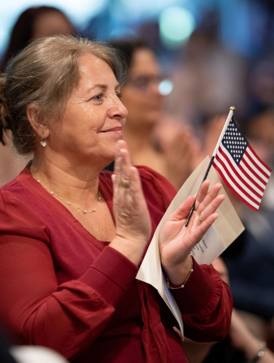 Close-up color photograph of woman in red blouse holding a small American flag and clapping