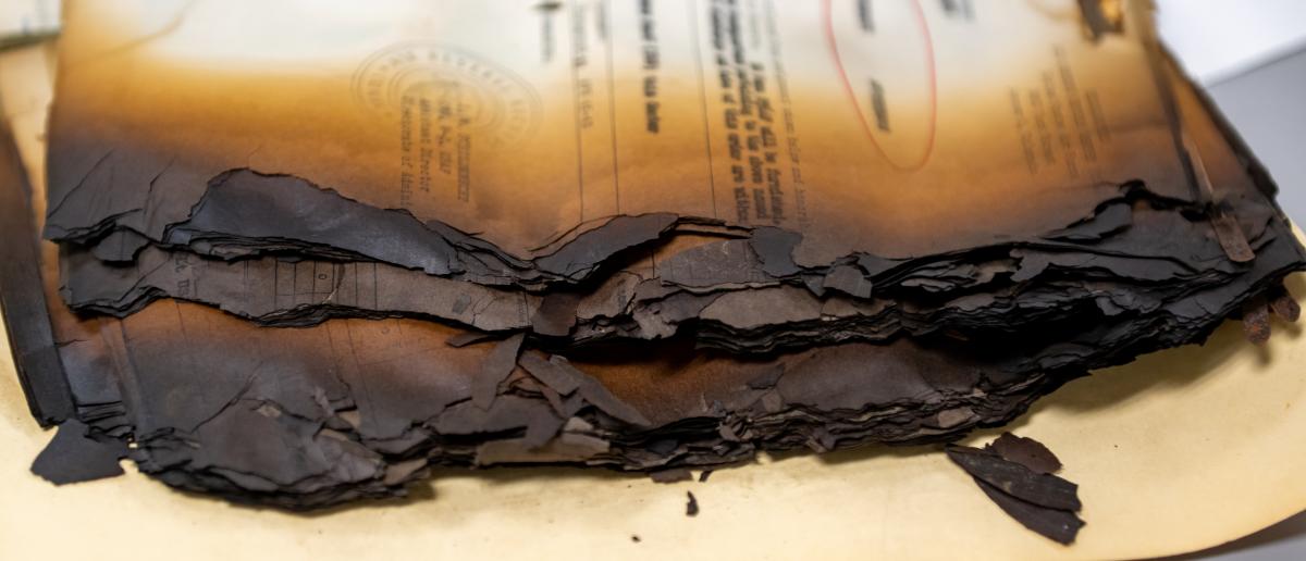 a color close-up photo of a stack of yellowed papers charred and crumbling along the edges