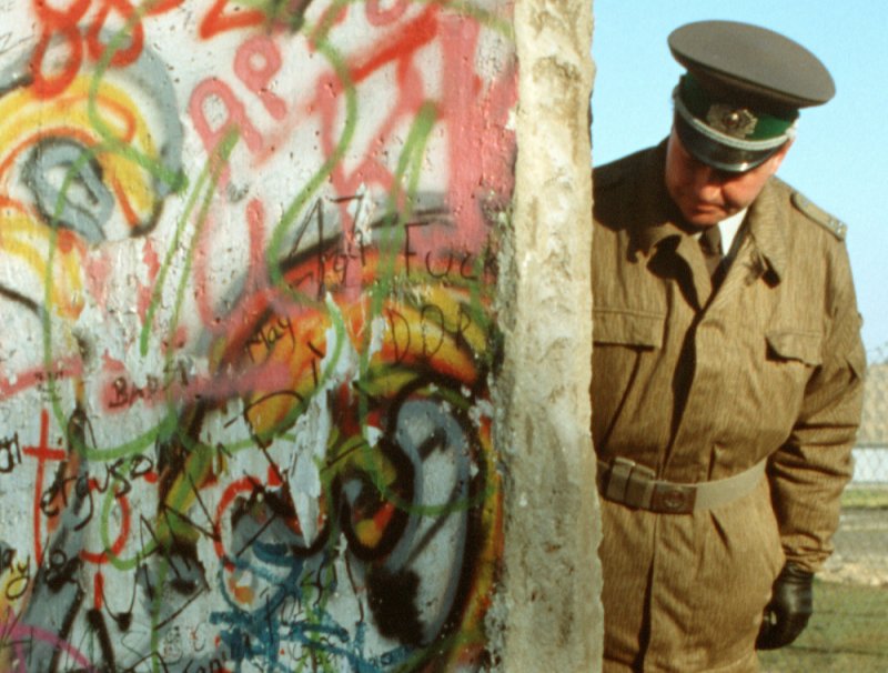 East German policeman looks at broken section of the Berlin Wall