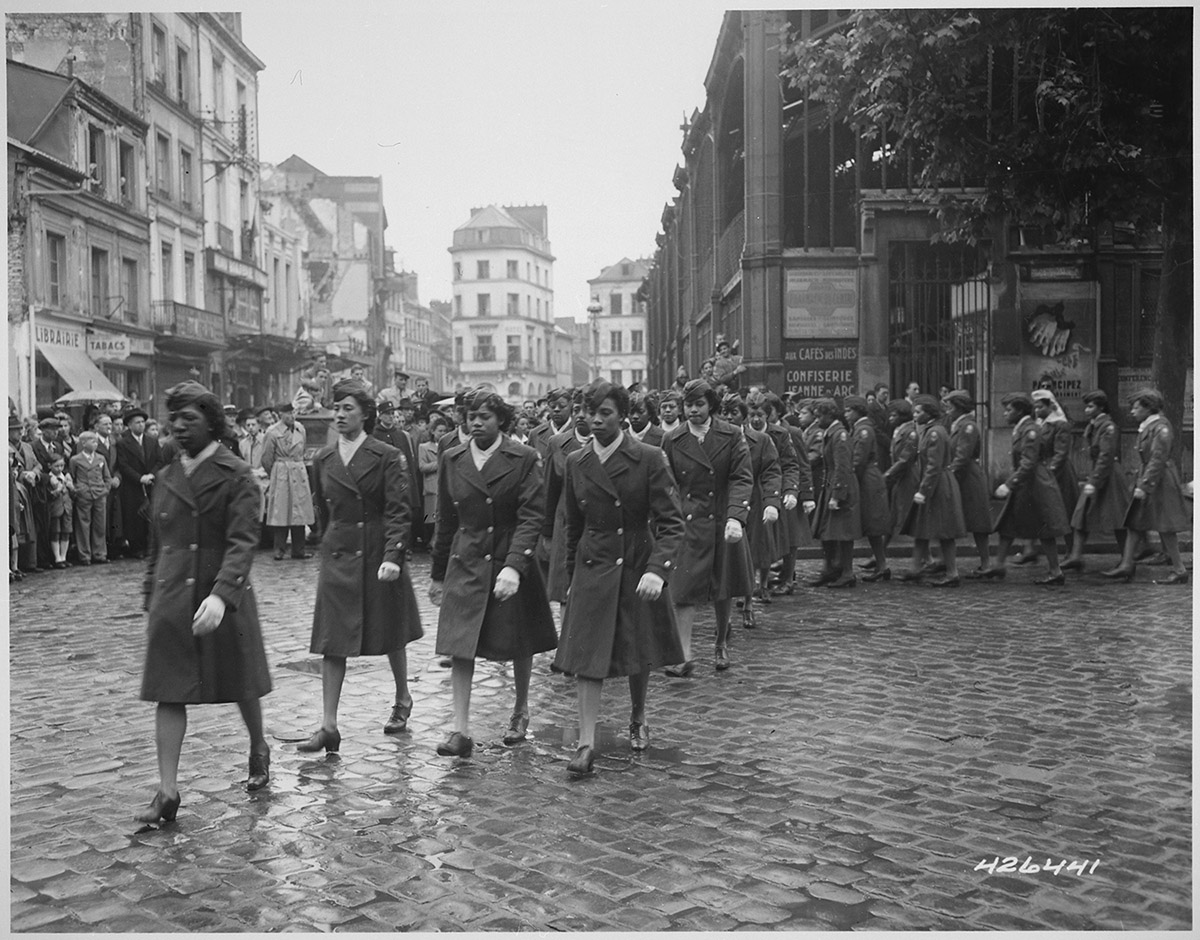 Black and white photograph of members of the 6888th Central Postal Directory Battalion in a parade ceremony in honor of Joan of Arc at the marketplace where she was burned at the stake. 