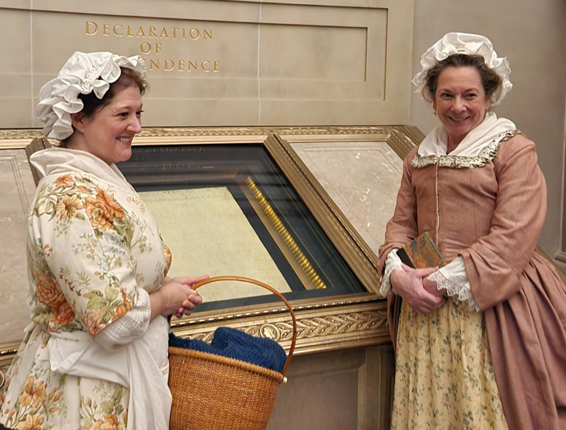 Reenactors portraying Sarah Fulton and Abigail Adams pose in front of the Declaration of Independence in the National Archives Rotunda