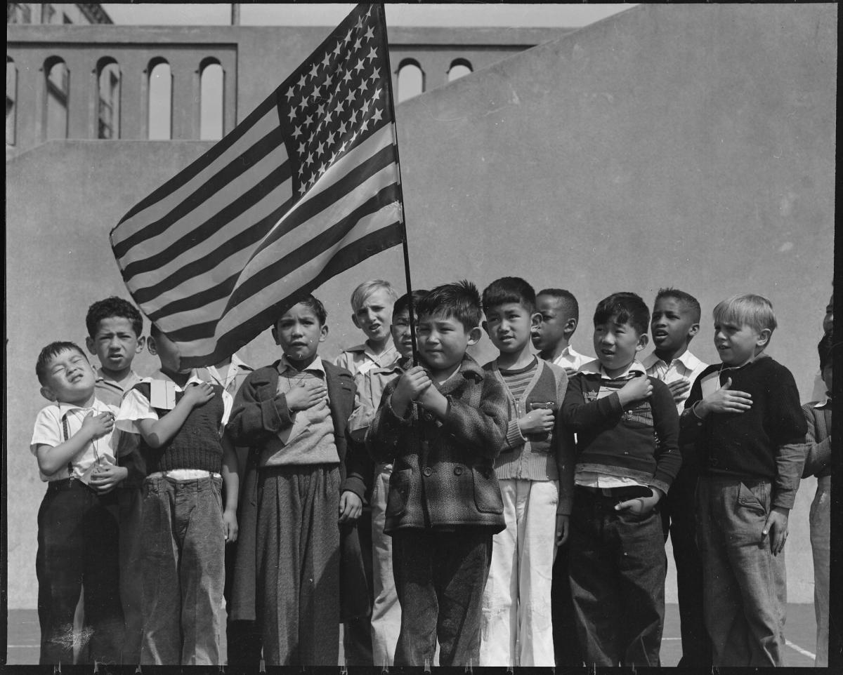 Children reciting pledge of allegiance under a flag at the Raphael Weill Public School. San Francisco, California.