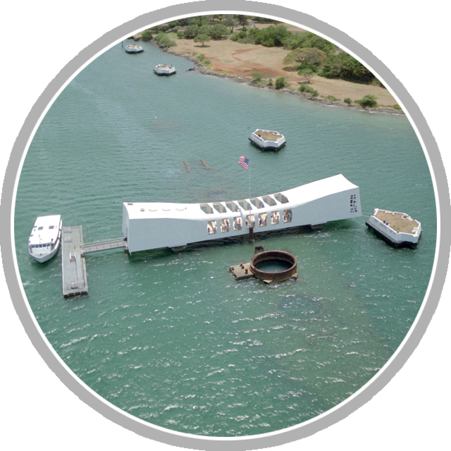 An aerial view of the USS ARIZONA Memorial at the northeast end of Ford Island, with markers in the background indicating battleships lost during the Japanese attack on Pearl Harbor on December 7, 1941